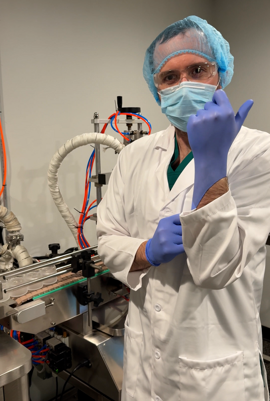 Amadeus Apothecary founder wearing protective clothing and gloves beside the facial cream filling line.