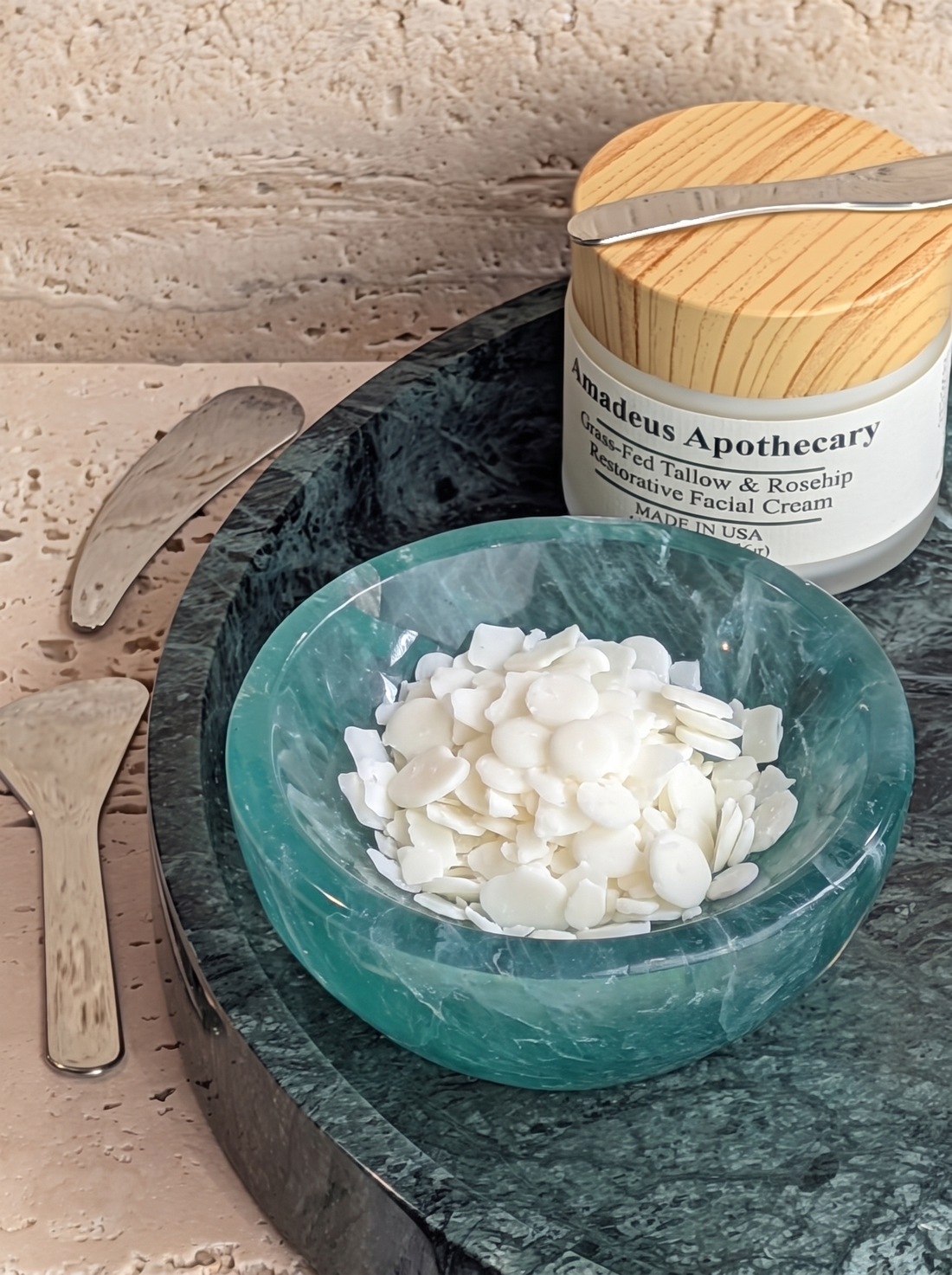 White cetyl alcohol pellets in a green bowl beside an Amadeus Apothecary facial cream jar.