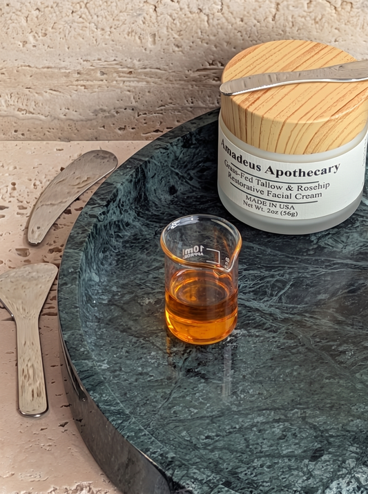 Rosehip seed oil in a glass beaker beside an Amadeus Apothecary facial cream jar.