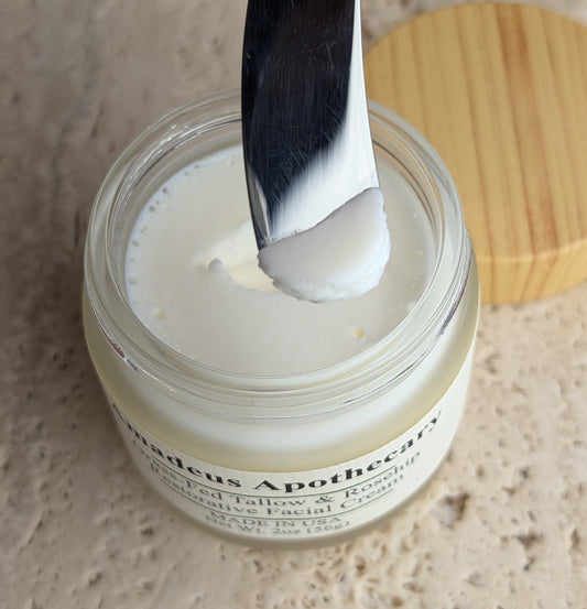 White facial cream on a metal spatula held above an open Amadeus Apothecary jar.