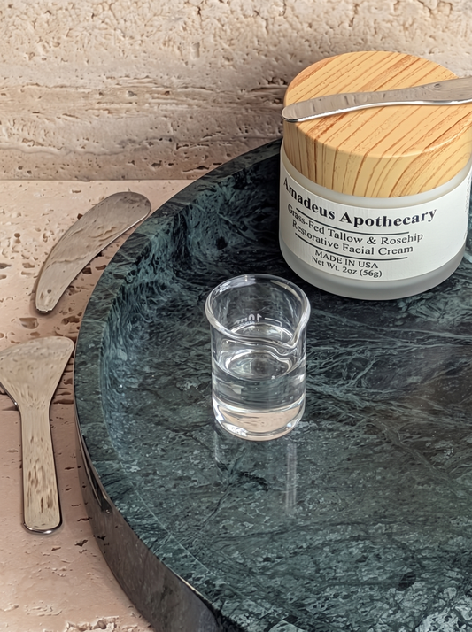 Vegetable glycerin in a clear glass beaker beside an Amadeus Apothecary facial cream jar.