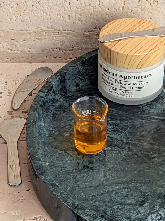Vitamin E oil in a glass beaker beside an Amadeus Apothecary facial cream jar.
